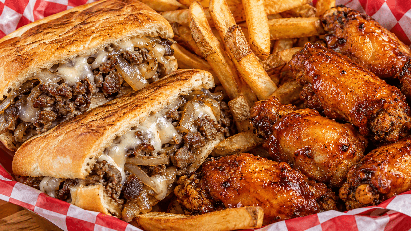 Illustrative Philly steak sandwich with fries and glazed chicken wings