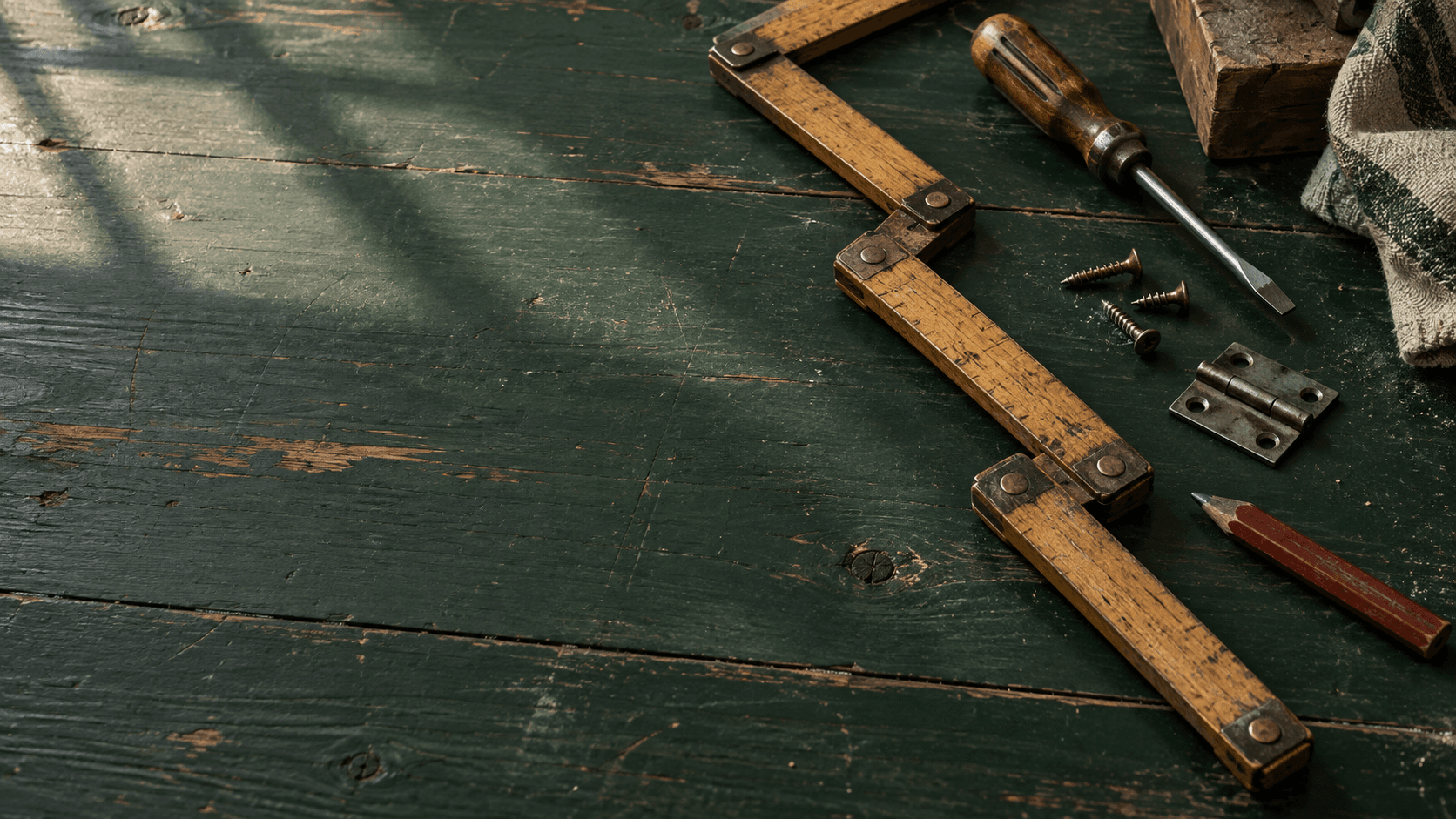 A folding wooden rule, screwdriver, hinge, and carpenter pencil on a green workbench
