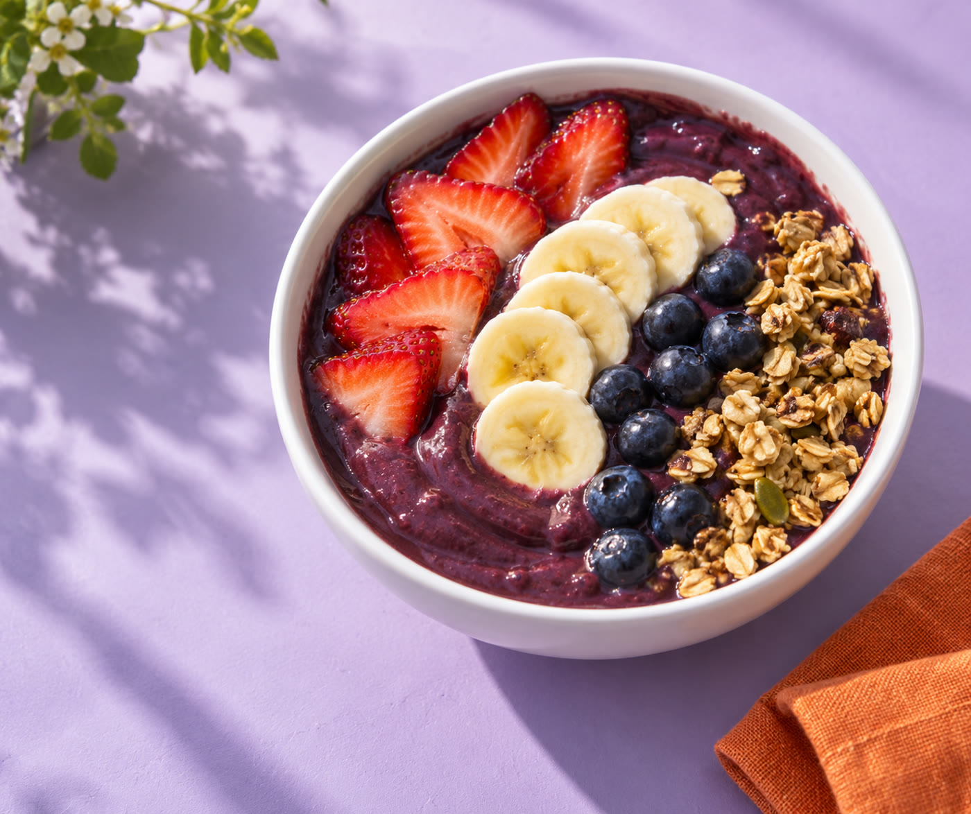 Purple açaí base with fresh strawberries, banana, blueberries and granola on a lavender table